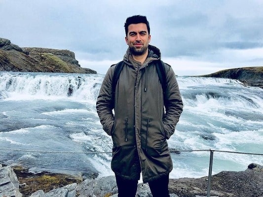 David Mumeni posing for a picture by wearing long green jacket and a black trouser.